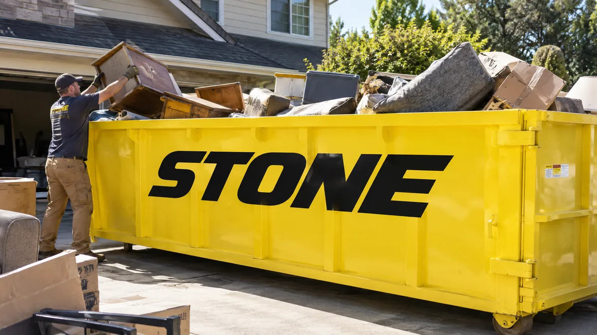 Worker loading household junk into a yellow STONE dumpster